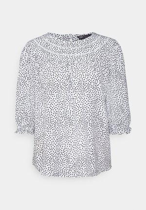 Blusa branca com bolinhas pretas, tecido translúcido, decote redondo, mangas 3/4 elásticas e pregas suaves para um ajuste descontraído.