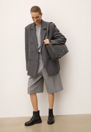 Blazer gris de doble botonadura, suéter gris, pantalones cortos gris ajustados y botas negras con cordones. Incluye un bolso de hombro negro con acentos dorados.