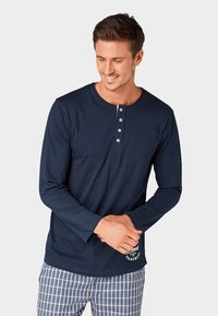 Navyblauwe T-shirt met lange mouwen en een ronde hals, drie-knops sluiting en bedrukt logo. Gecombineerd met shorts met een geruit patroon. Gladde textuur.