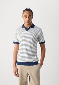 Polo rayé blanc avec des accents bleu marine. Doté d'un col et de manches courtes, fabriqué en tissu texturé, avec une coupe légèrement ample.