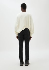 Sweatshirt oversize crème, pantalon noir ajusté, et chaussures grises à brides. Tissu lisse, coupe décontractée, et design minimaliste.