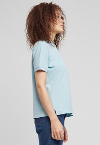 Šviesiai mėlyna trumpomis rankovėmis marškinėliai su laisvu prigludimu, šoninėmis skeltukėmis ir apvalia iškirpte, pagaminti iš minkštos medvilninės medžiagos.