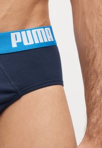 Männlicher Oberkörper trägt marineblaue Slips mit einem blauen Bund, auf dem linken Seite mit dem weißen Puma-Logo.