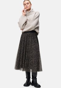 Beige ribbet turtleneck sweater parret med en sort leopardprint tulle midi nederdel og sorte ankelstøvler med en kraftig sål.