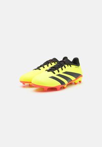 Scarpe da calcio gialle con strisce nere e lacci neri, dotate di una parte superiore testurizzata e una suola di un vivace rosa. Progettate per una migliore aderenza sull'erba.