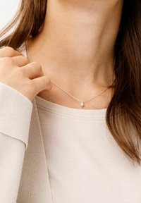 Srebrny naszyjnik z delikatnym łańcuszkiem i małym, owalnym wisiorkiem, noszony na jasnym swetrze.