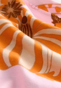 Bomuldsstof med et blomstermønster i orange og brunt på en lyserød baggrund, med glat tekstur og blide folder.