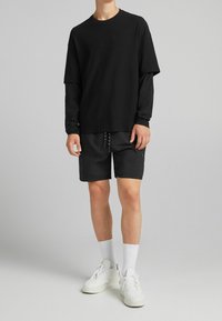 Černé oversized tričko s krátkým rukávem, přes které je oblečeno černé tričko s dlouhým rukávem, spojené s černými šortkami a bílými teniskami.