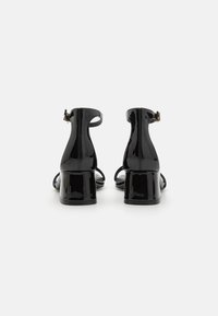 Sandali con tacco a blocco in vernice nera, con cinturino alla caviglia, punta aperta e finitura lucida; dotati di zip posteriore e design minimalista.