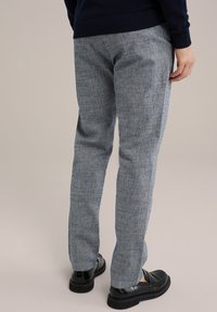 Šviesiai pilkos, tekstūruotos kelnės, pagamintos iš audinio, su tiesia kojų fasonu. Nešiojamos su juodais loaferiais kontrastui.