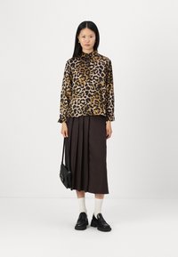 Leopard print blouse in beige and black, long sleeves, paired with a brown pleated midi skirt. Complete with black loafers and a small black bag.