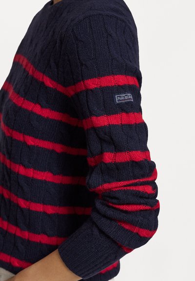 Pull tricot à rayures bleu marine et rouge avec des poignets côtelés. Dispose d'une texture en tricot à cable et d'un logo 'Polo RL' sur la manche.