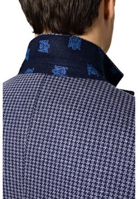 Marynarski niebieski płaszcz w wzór houndstooth z kontrastowym ciemnym kołnierzem zdobionym niebieskim kwiatowym wzorem. Gładka tekstura, dopasowany krój.