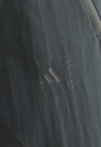 Nahaufnahme eines dunklen Stoffs mit geprägtetem Adidas-Logo und kreisförmigem Text mit der Aufschrift "Stella McCartney Next".