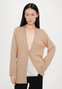 Beige kötött kardigán texturált mintával, V-kivágással, nyitott elülső résszel, egy gombos záródással és bordás mandzsettákkal.