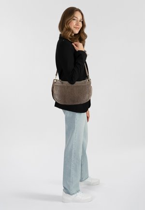 Braune, geflochtene Handtasche mit glattem Lederbesatz. Sie hat eine strukturierte, abgerundete Form und einen verstellbaren Schulterriemen. Getragen mit hellen Jeans und weißen Sneakers.