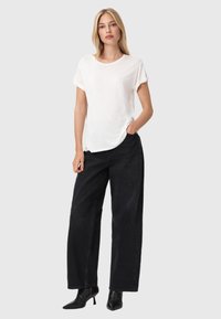 T-shirt bianco a maniche corte abbinato a jeans neri a gamba larga con vita alta. Tessuto morbido con una vestibilità rilassata, che mette in mostra un design semplice.