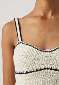 Top lavorato a maglia in crema con un motivo testurizzato, caratterizzato da dettagli neri lungo le spalline e il collo, con una silhouette aderente.