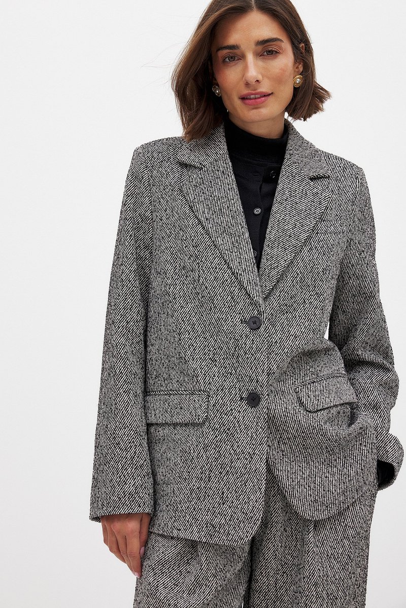 Gray houndstooth blazer with a notched collar, two front pockets, and a single button closure. Material is textured with visible weave details.