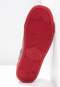 Semelle de sneaker rouge en caoutchouc avec des motifs texturés et le logo "DIESEL" embouti, présentant des formes géométriques et un design de semelle proéminent.