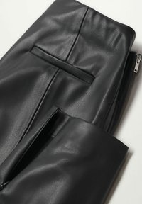 Černé kožené kalhoty s texturovaným povrchem, které mají horizontální šev a zipové rozparky na kotnících.