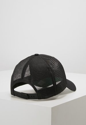 Casquette de baseball noire en mesh avec bride snapback réglable posée sur une surface blanche sur fond gris clair.