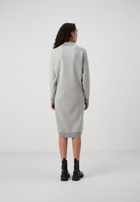 Robe tricotée grise avec un motif géométrique, manches longues, longueur mi-mollet, et accents côtelés au col et à l'ourlet, associée à des bottes noires.