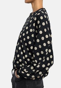 Czarna bluza z dużymi beżowymi kropkami, okrągły dekolt, długie rękawy oraz luźny krój. Tkanina wydaje się miękka o gładkiej teksturze.