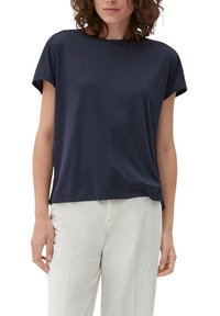 Löysä istuvuus, pyöreä pääntie, lyhythihainen tummansininen paita. Pehmeää kangasta, jossa on hienoinen rakenne ja näkyvät saumarivit. Yhdistetty vaaleisiin housuihin.