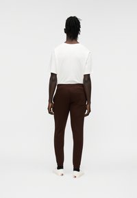 Καφέ φόρμες με εφαρμοστή σχεδίαση, ελαστική μέση και πίσω τσέπη, συνδυασμένες με άσπρο εφαρμοστό T-shirt και άσπρα παπούτσια.