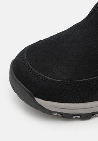 Bottine cheville en suède noir avec une surface texturée, un bout arrondi et une semelle en caoutchouc gris dotée de relief pour une meilleure adhérence. Détails de couture subtils visibles.