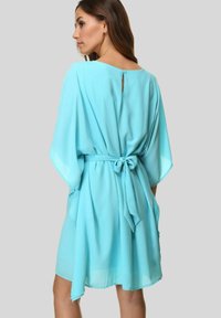 Un vestido fluido de color azul claro, hecho de una tela transparente, con mangas amplias y un lazo en la cintura, y un pequeño botón en la parte posterior.