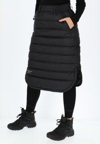 Black insulated skirt with horizontal stitching, elastic waistband, and side pockets. Worn over black leggings and rugged black boots.