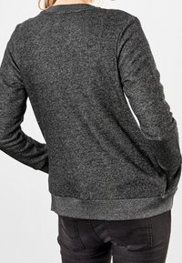 Szary sweatshirt z okrągłym dekoltem i długimi rękawami, wykonany z teksturowanej tkaniny. Posiada ribbowane wykończenia u dołu i na rękawach. Tylny widok ukazuje dopasowany krój.