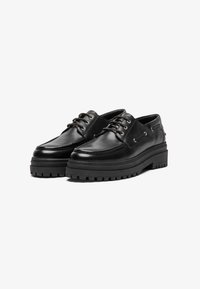 Zapatos de cuero negro con punta redondeada, suela de goma gruesa con dibujo, y cierre de cordones dual con ojales de metal.