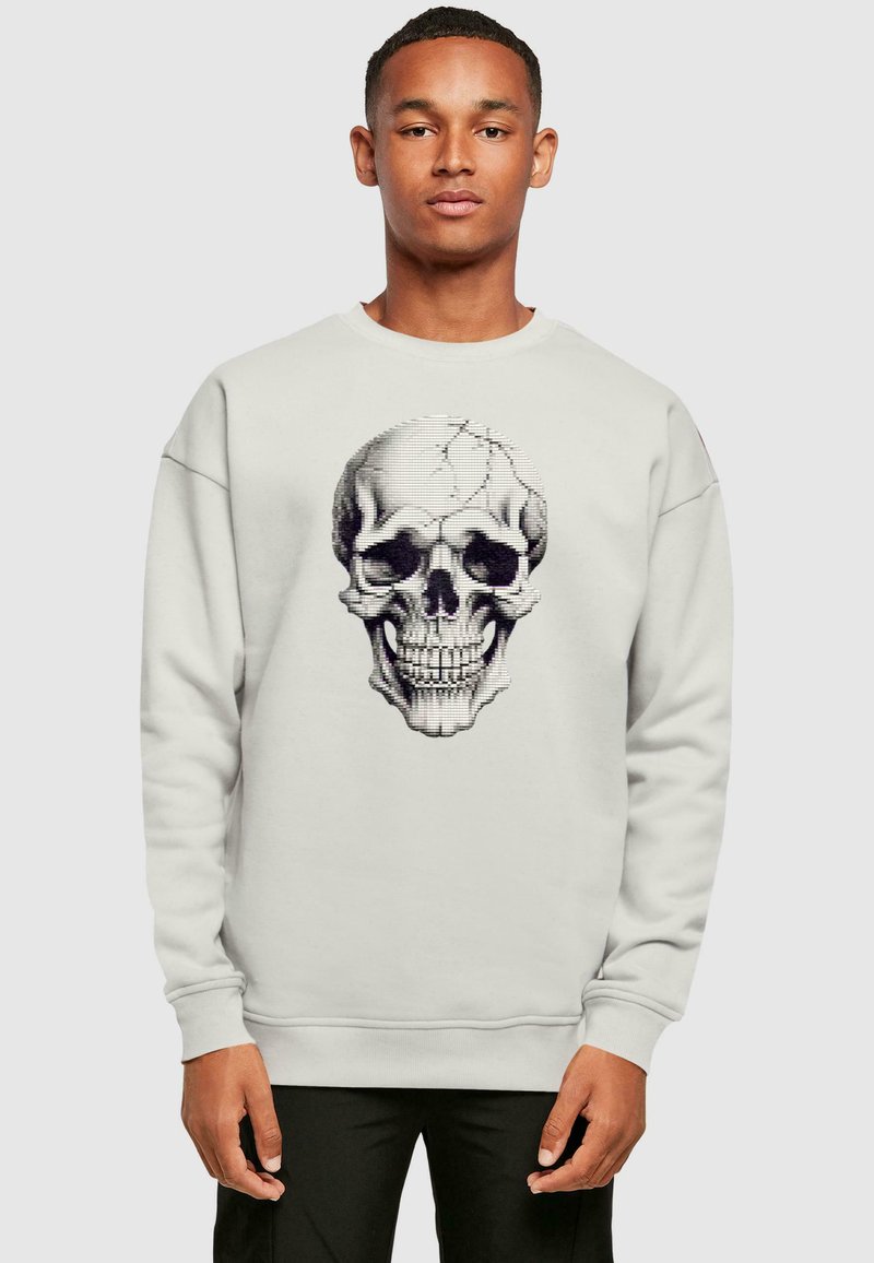 Sweatshirt gris clair avec un motif détaillé de skull noir sur le devant. Le tissu est doux, avec des poignets et un ourlet côtelés.