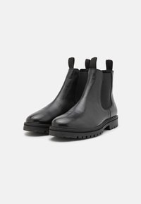 Botas Chelsea de cuero negro con paneles laterales elásticos, tiradores y suelas de goma texturizada para mayor agarre. Acabado suave y diseño de puntera redondeada.