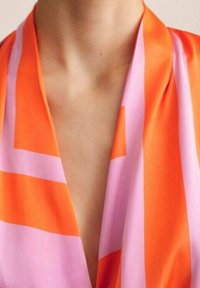 Haut cache-cœur coloré présentant des rayures orange vif et rose clair, fabriqué en tissu lisse avec un col en V, mettant en valeur une finition soignée.