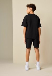 Camiseta negra de manga corta y pantalones cortos a juego con un ajuste cómodo. El conjunto se combina con zapatillas blancas y calcetines blancos hasta el tobillo.