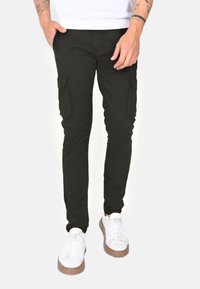Pantaloni cargo neri con tasche laterali, design slim-fit, realizzati in tessuto misto cotone. Abbinati a sneakers bianche con suola marrone.