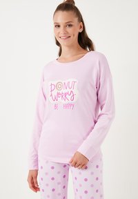 Világos rózsaszín, hosszú ujjú ing, amelyen a "DONUT WORRY BE HAPPY" grafika látható, világos rózsaszín nadrággal párosítva, lila pöttyökkel díszítve. Puha anyag.