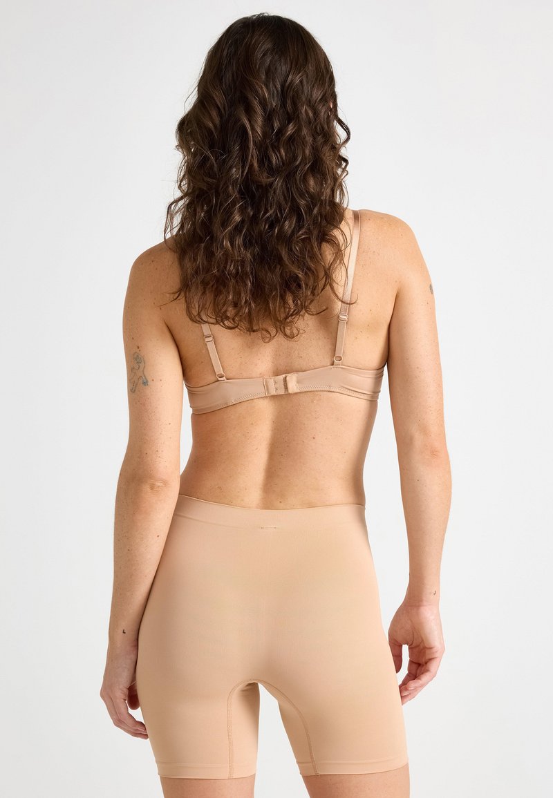 Nude seamless bra with adjustable straps and a hook closure, paired with matching high-waisted shorts, both featuring a smooth, stretchy texture.