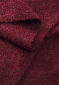 Bordo veltinio audinys su švelniu tekstūromis, šiek tiek pūkuotas paviršius, sluoksniuojamas ir persidengiantis natūralioje, drabuota pozicijoje.