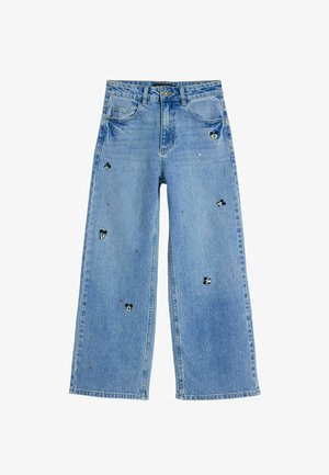 Jeans de denim de color azul claro, de pierna ancha, con diseños de personajes bordados, adornos plateados y una configuración clásica de cinco bolsillos.