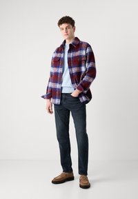 Καρό πουκάμισο σε κόκκινο, μπλε και λευκό, με δύο τσέπες στο στήθος και κουμπιά. Συνδυασμένο με ανοιχτό μπλε πουλόβερ, σκούρα τζιν και καφέ loafers.