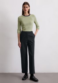 Ribbed green knit top with a dark neckline, paired with black tailored pants. Black loafers complete the look. Simple and sleek design.