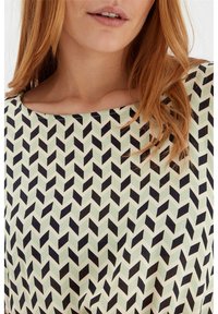 Gemusterte Bluse in Hellgrün mit schwarzem Chevron-Design. Weicher Stoff mit weitem Ausschnitt und glatter Textur.