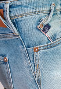Lichtblauwe denim jeans met een vervaagde afwerking, voorzien van bruine stiksels, koperen nieten en een small merklabel op de voorzak.