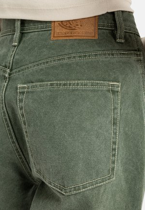 Groene denim broek met een achterzak, contrasterende stiksels en een leren merklabel in bruin op de tailleband.