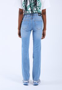 Jeans de tiro alto en azul claro con un diseño de pierna recta, cinco bolsillos y detalles de costura sutiles, combinados con una camiseta gráfica blanca.